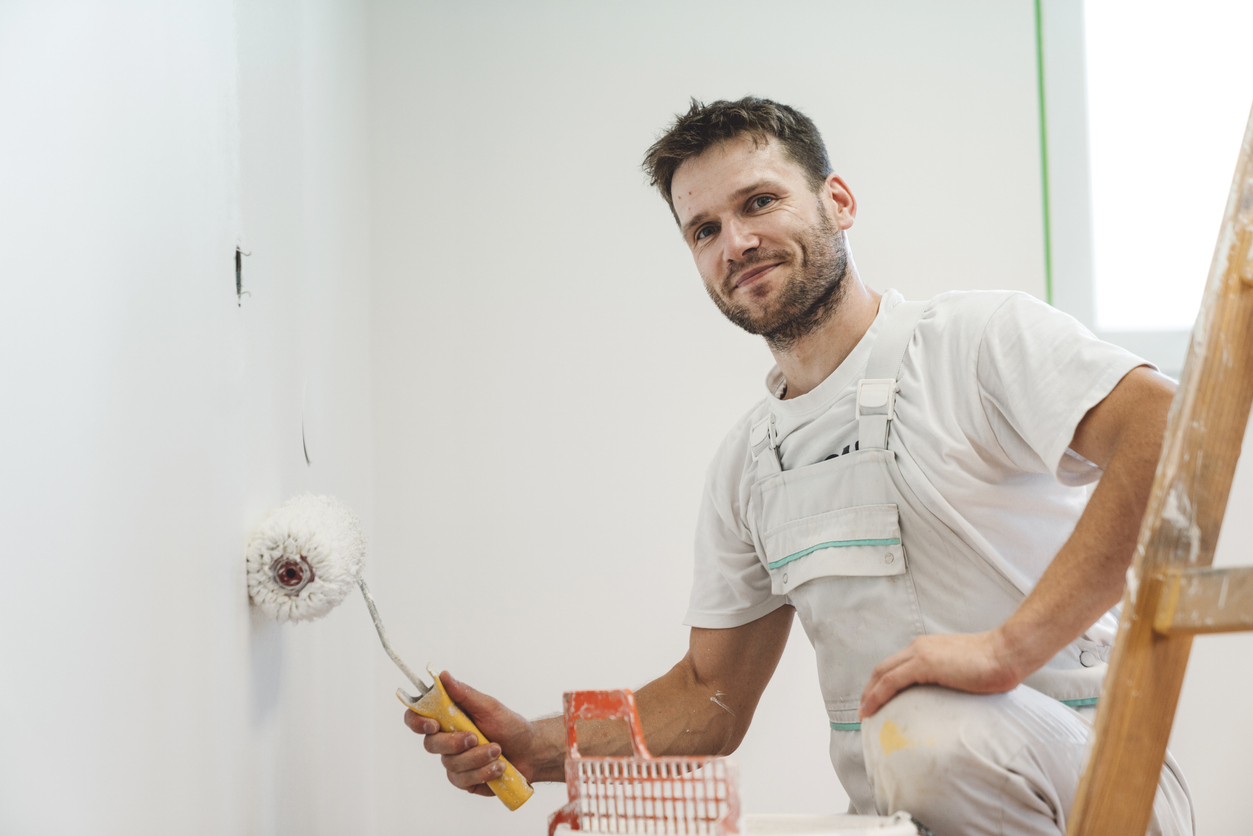 Smiling man holding a paint roller against the wall
