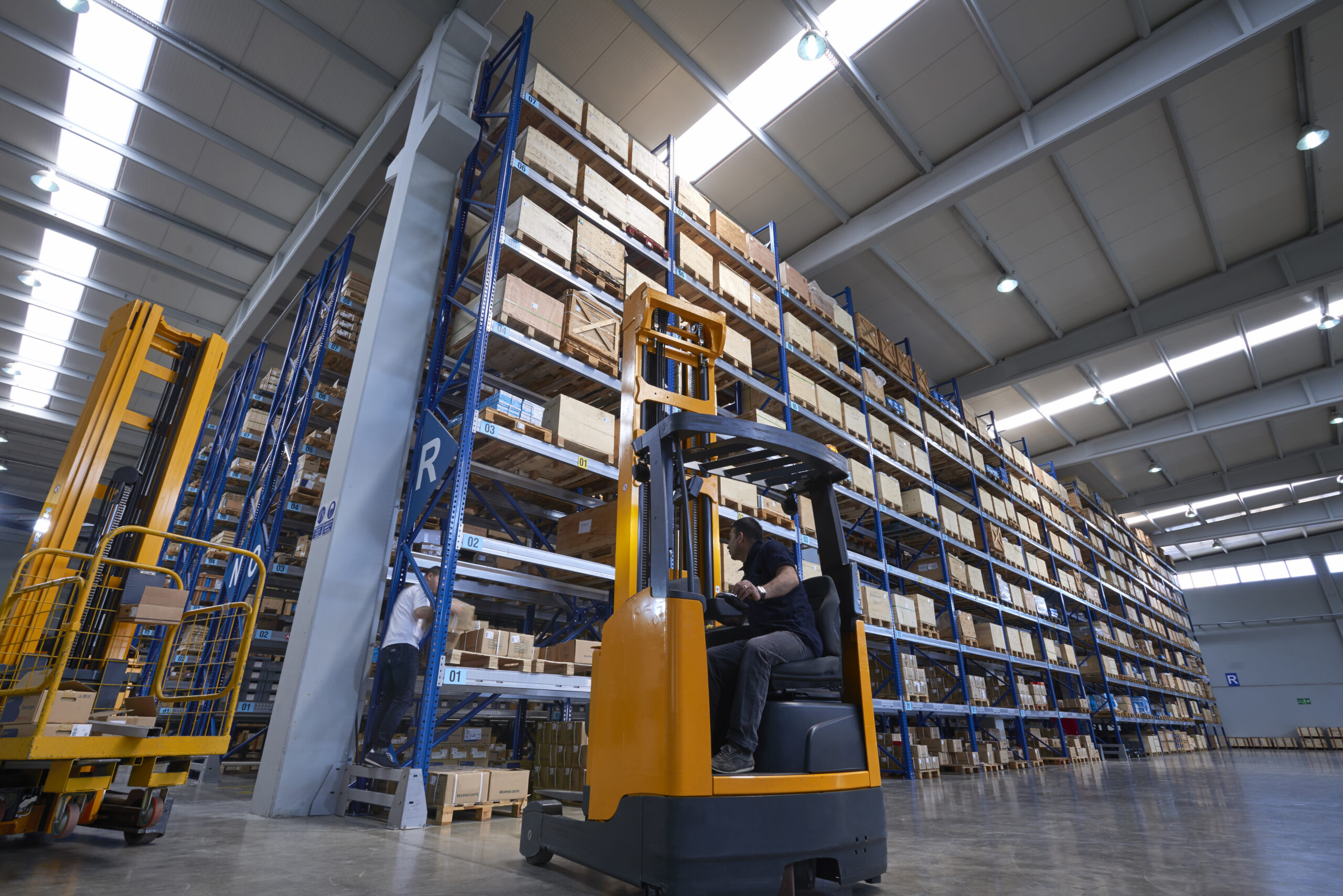 Forklifts carrying cardboard box in warehouse.